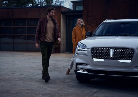 A man and a woman approaching a 2024 Lincoln Aviator® SUV, which illuminates certain lights when they are close | Brinson Lincoln of Athens in Athens TX